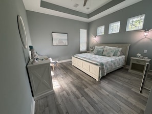 Une chambre à coucher comprenant un lit, des tables de chevet, une commode, une fenêtre et un tableau accroché au mur.