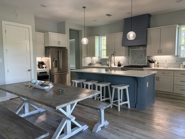 A modern kitchen with a central island, white cabinetry, stainless steel appliances, and pendant lighting.