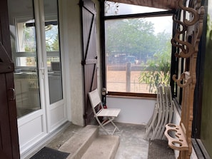 A room with a sliding glass door, a small folding chair, a wooden bench, and a view of an outdoor area with trees and a fence.