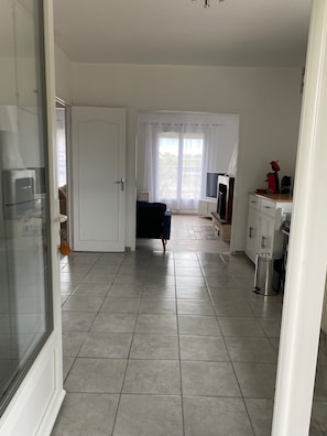 A spacious living area with a large window, a television, and a kitchenette.