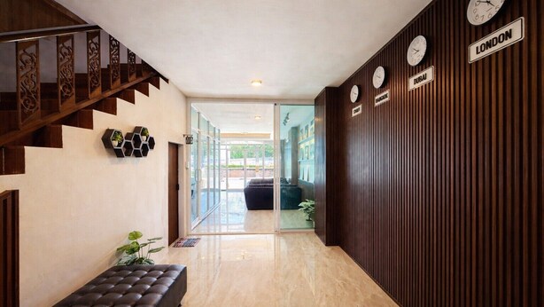 A hotel lobby with a staircase, a bench, a reception desk, and clocks indicating different cities. - Henry's House (Wichit)