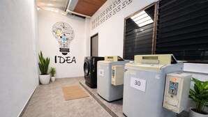 A laundry area with three washing machines, a wall-mounted sign with the word 'IDEA,' and potted plants. - Henry's House (Wichit)