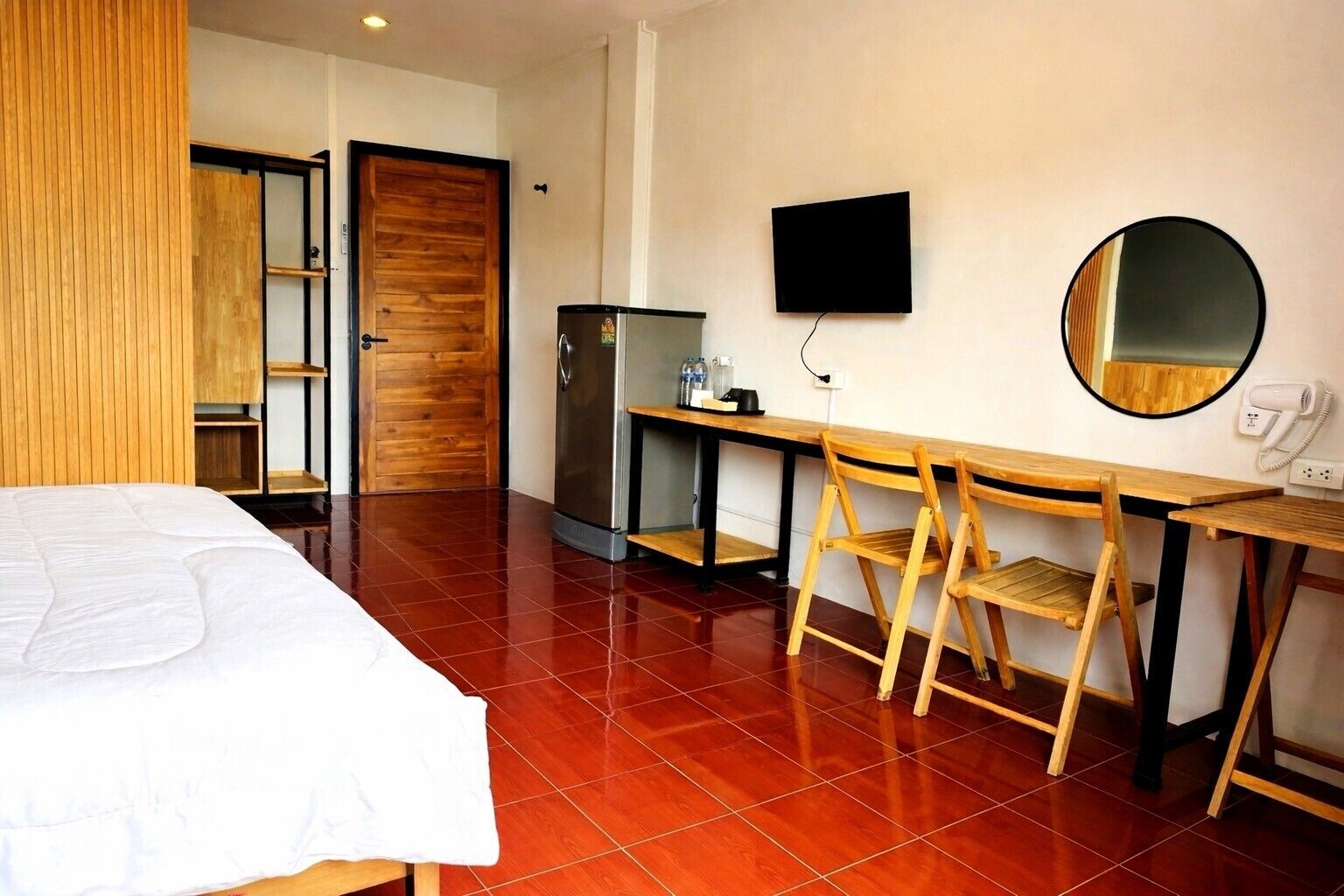 A hotel room with a bed, a desk with chairs, a refrigerator, a TV, and a mirror.
