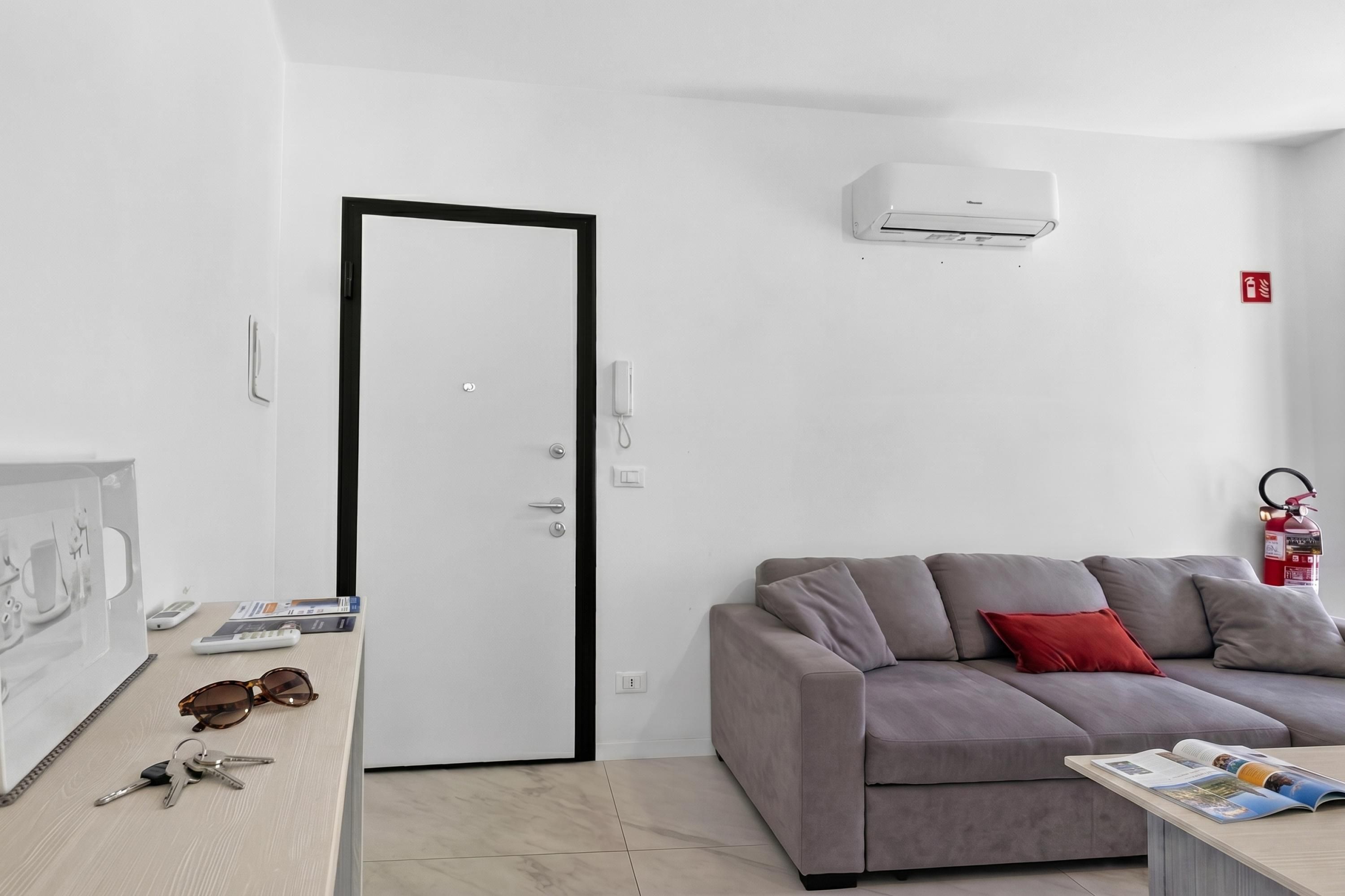 A modern living room with a grey sofa, a coffee table, a door, and an air conditioning unit.