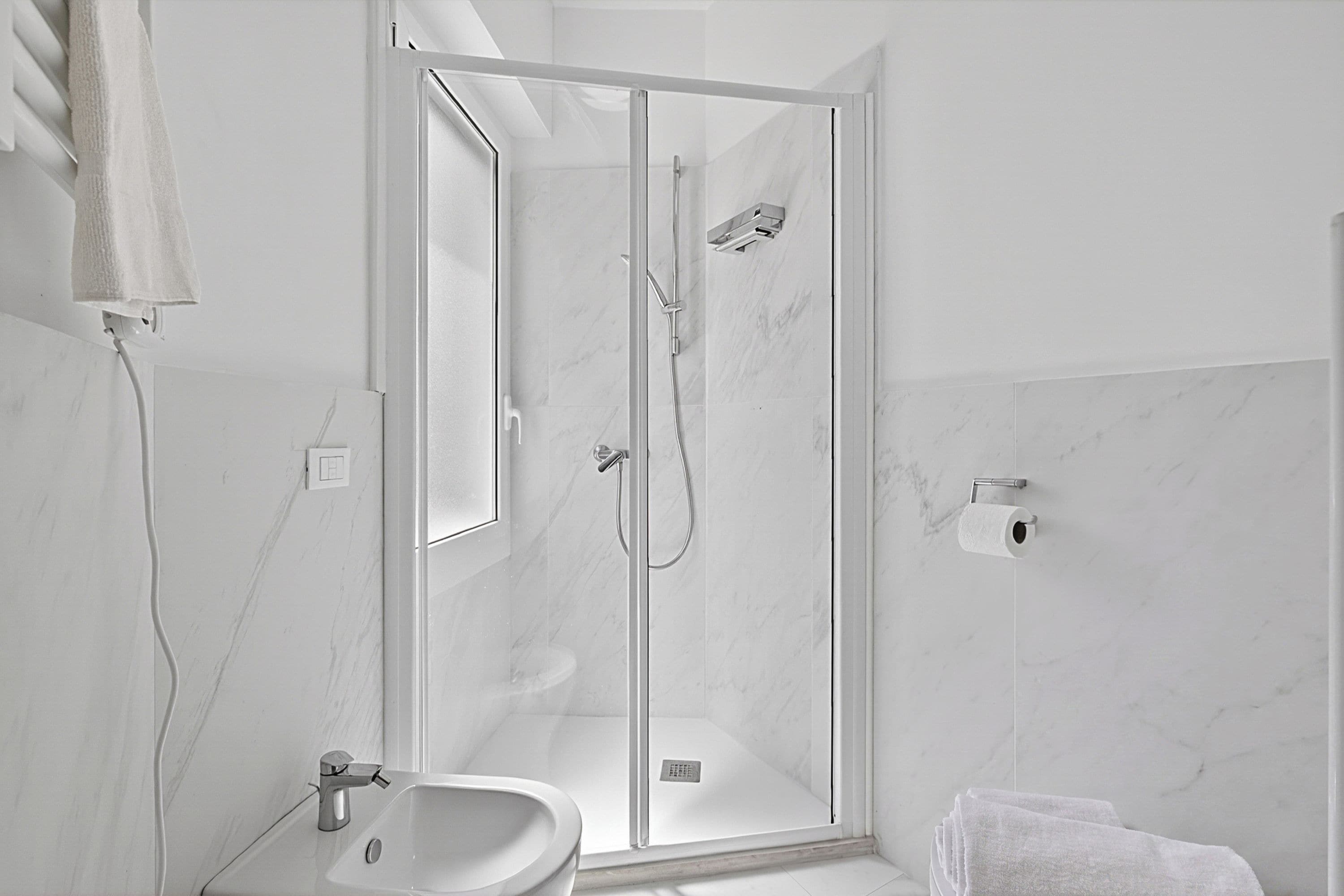 A modern bathroom with a glass-enclosed shower, a sink, and a toilet paper holder.