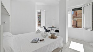 Ein heller Raum mit einem Bett, einer Zeitschrift, Sonnenbrillen, einem Hut und einem kleinen Tisch mit einem Stuhl.