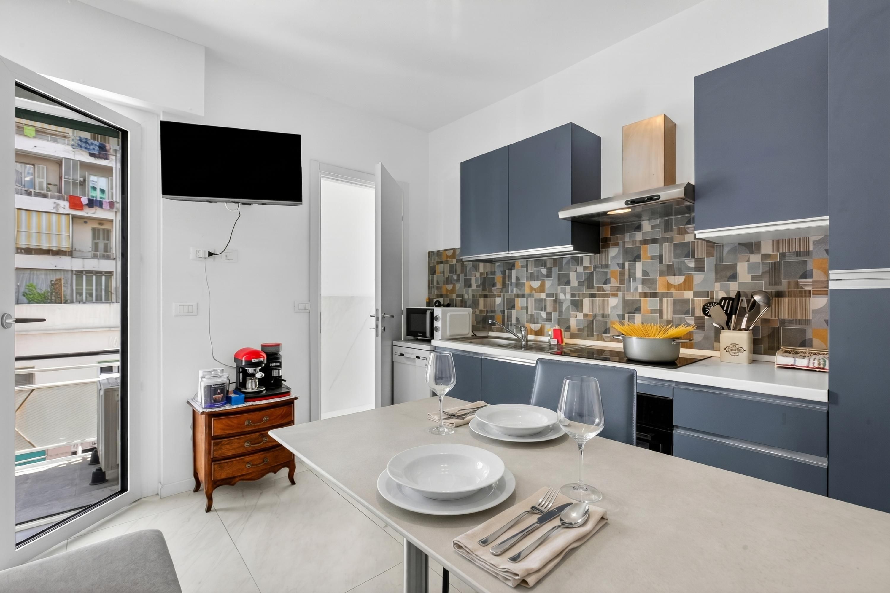 Une cuisine moderne avec des meubles gris, un pare-feu en carreaux et un coin repas avec une table dressée pour deux personnes.