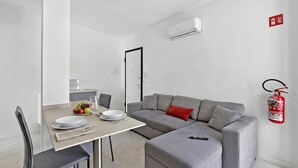 Ein moderner Wohnraum mit Essbereich, grauem Sofa und einem Feuerlöscher an der Wand.