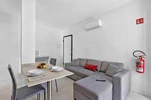 A modern living space with a dining area, grey sofa, and a fire extinguisher on the wall. - Emilia Sweet - With Balcony + AC (Sanremo)