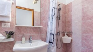 Un baño con lavamanos, espejo, ducha y perchero.
