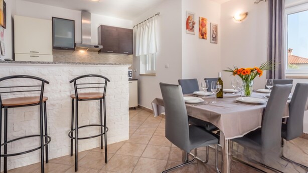 Una cocina moderna con una isla central, taburetes de bar y un comedor con una mesa dispuesta para cuatro.