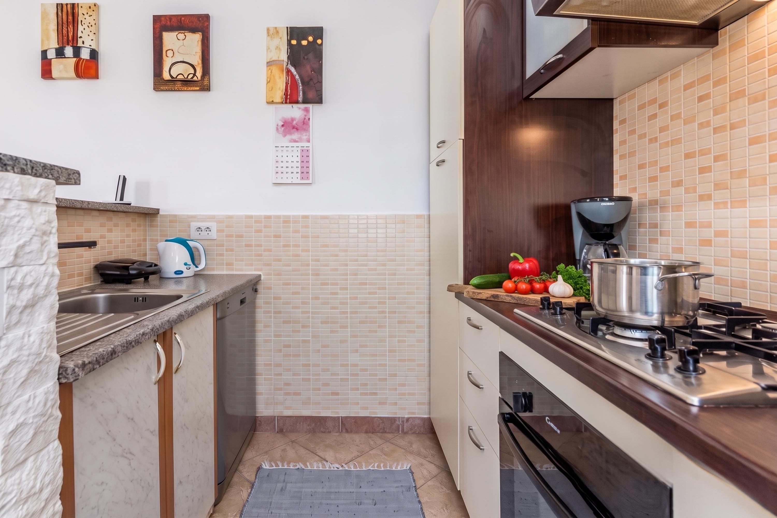 A modern kitchen with a gas stove, a coffee maker, and a calendar on the wall.