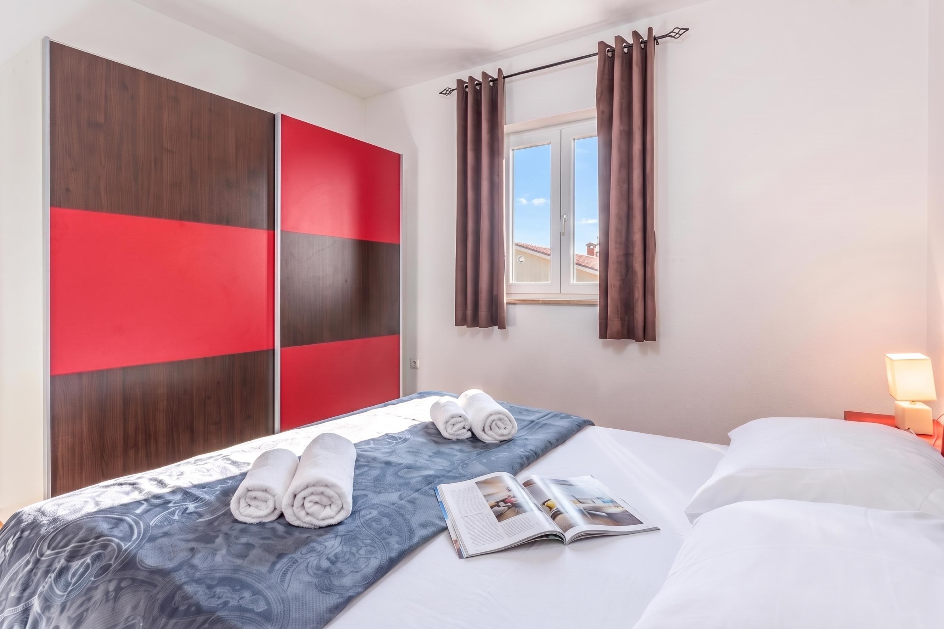 Quarto de hotel com cama, guarda-roupa, janela com cortinas e luminária de cabeceira.