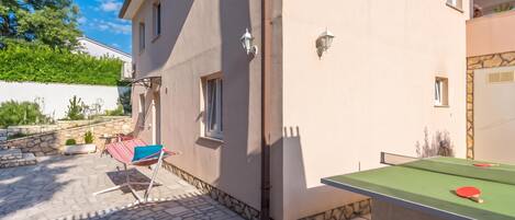A building with a stone patio, a ping pong table, and a hammock.