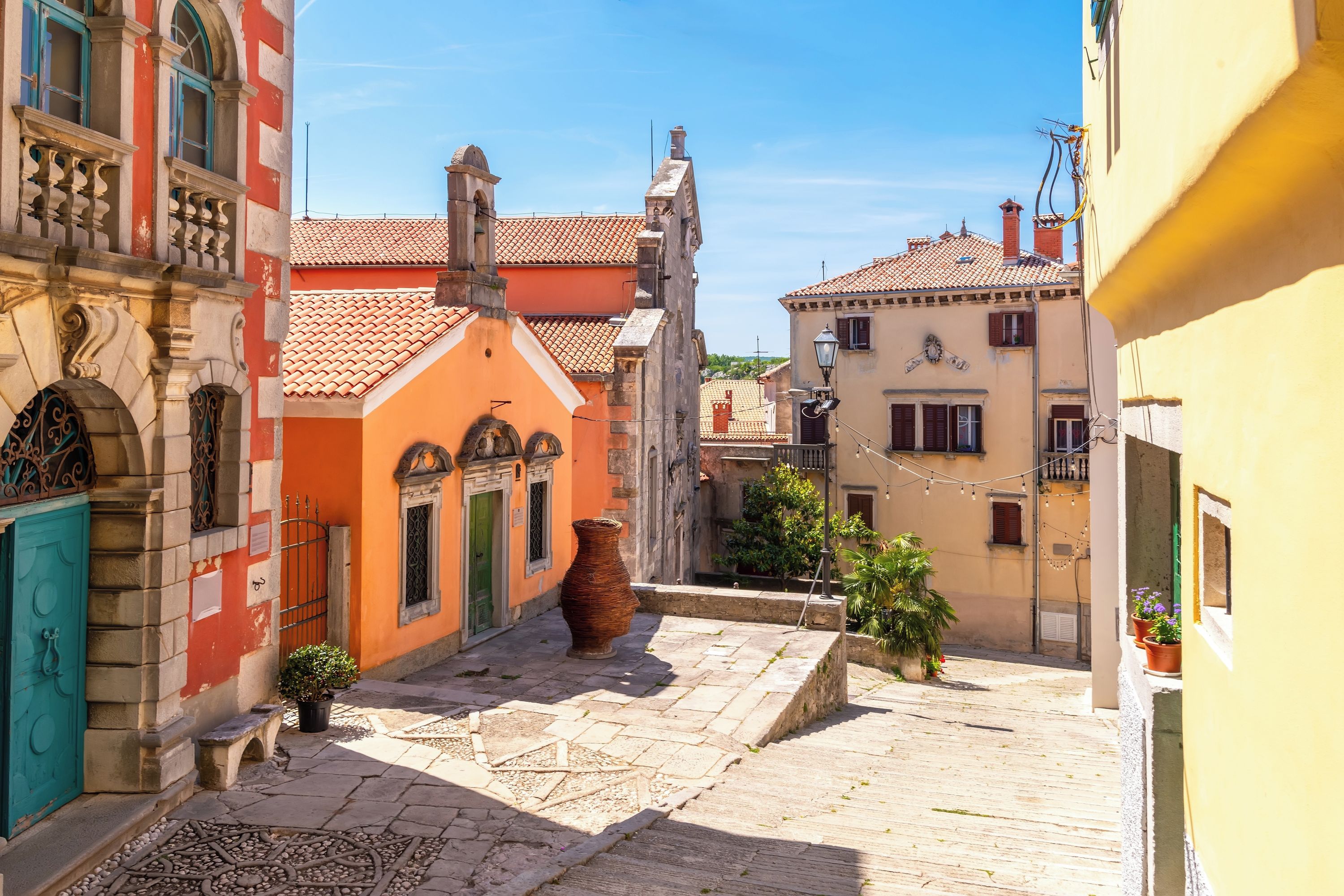 Una calle estrecha con edificios históricos, una maceta de cerámica grande y plantas en macetas.