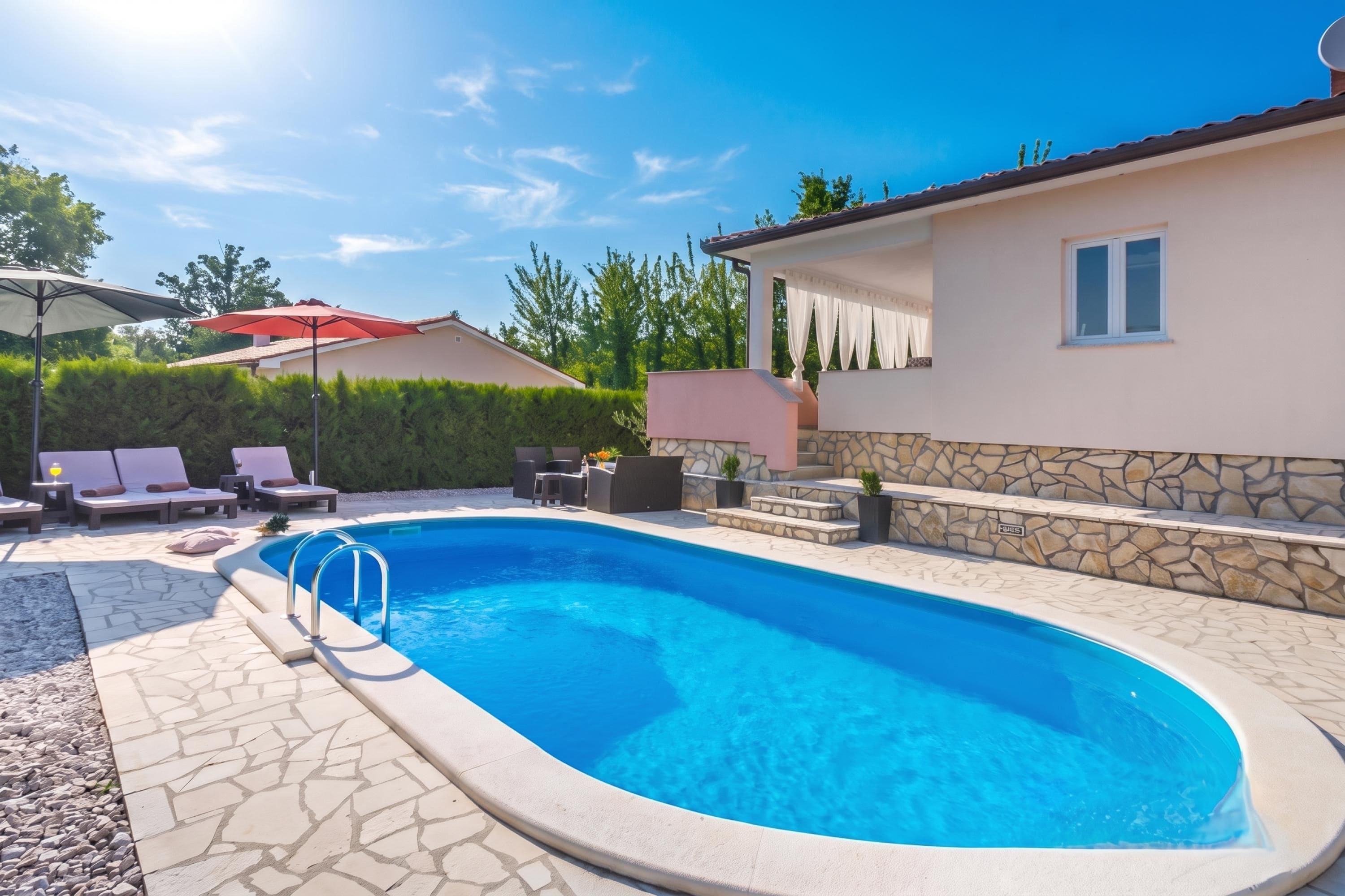A swimming pool with a stone wall and a lounge area with chairs and an umbrella.
