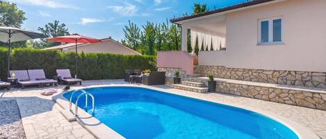 A swimming pool with a stone wall and a lounge area with chairs and an umbrella.