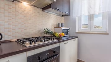 A kitchen with a gas stove, oven, microwave, and a window with a view.
