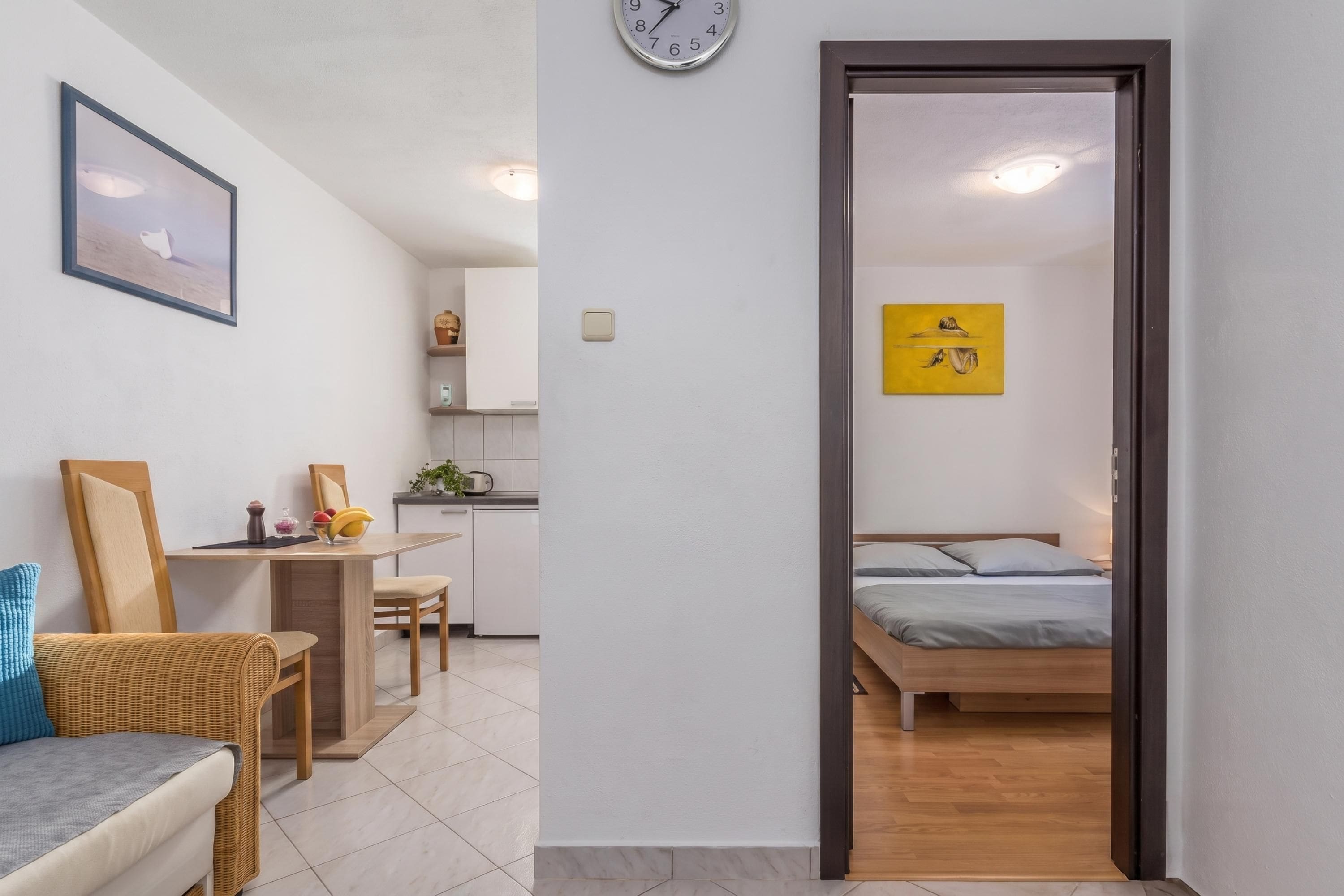 A room with a bed, a desk, a chair, a clock, and a painting on the wall.