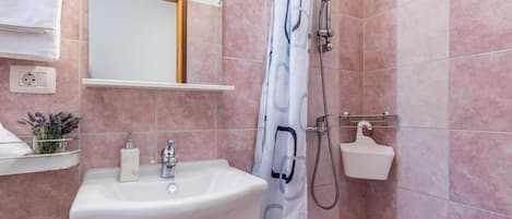 Un baño con lavamanos, espejo, ducha y perchero.