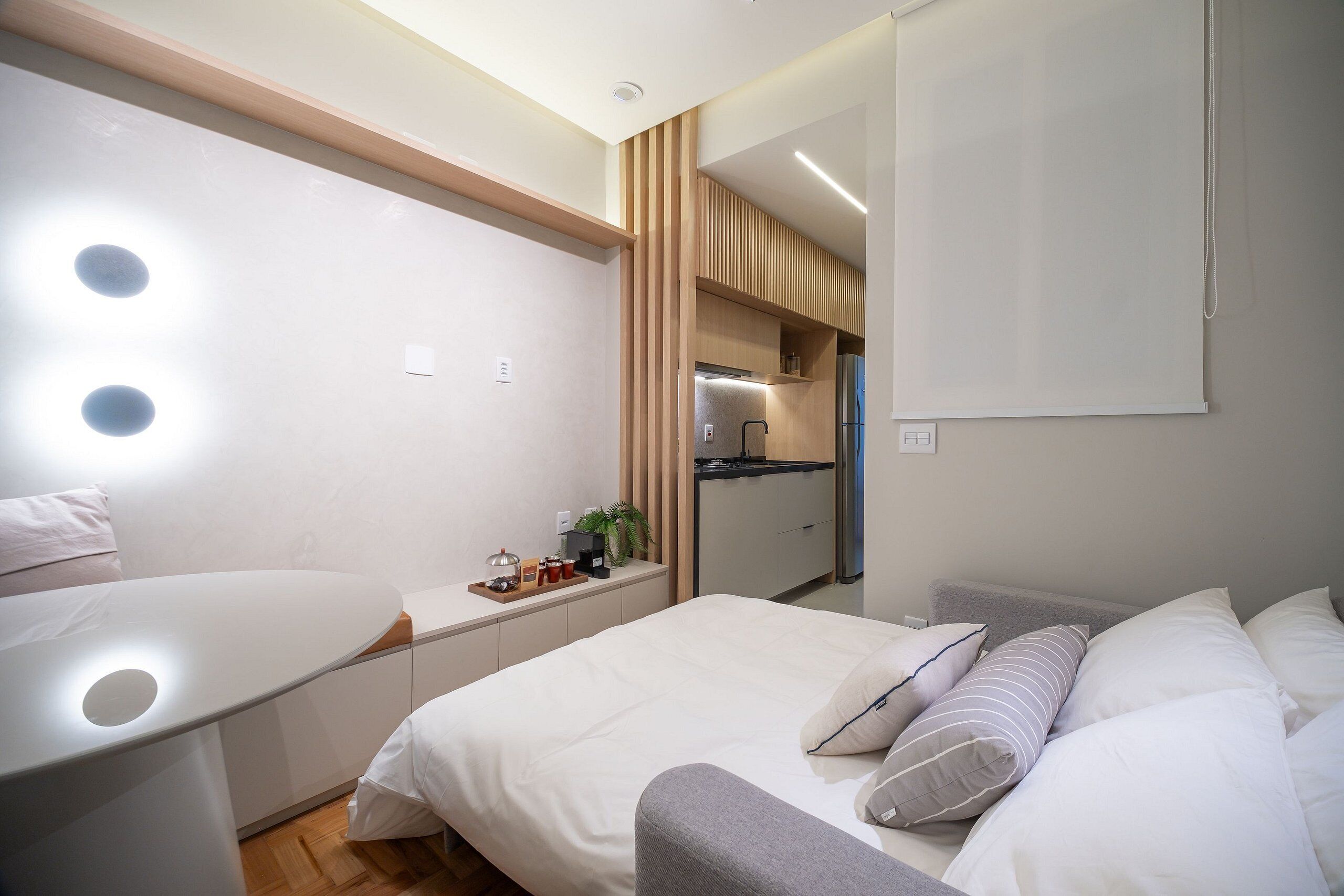 A modern bedroom with a bed, bedside table, and a small kitchenette area.