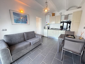 A modern living room with a grey sofa, a dining table with a tray, and a kitchen area with cabinets and appliances. - Agi Joan Margarit 24 Casa for rent in Roses Girona. (Roses)