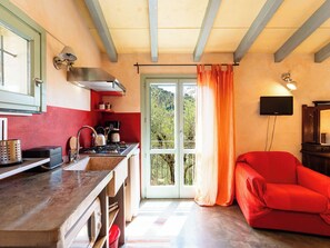 Eine Küche mit Herd, Spüle und einem roten Sofa in einem Raum mit großem Fenster und Fernseher.