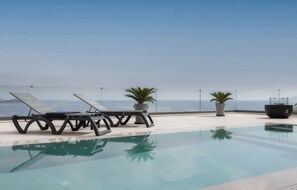 Ein Infinity-Pool auf dem Dach mit Liegestühlen und Topfpflanzen.