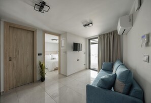 Ein modernes Wohnzimmer mit einer Couch, einem Fernseher und einer Tür zum Schlafzimmer.