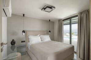 Ein modernes Hotelzimmer mit einem großen Bett, einem Glastisch, einer Wandleuchte und Blick auf einen Swimmingpool.