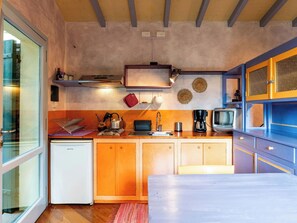 Eine kleine Küche mit Holzausstattung, einem Kühlschrank, einer Kaffeemaschine und einem alten Fernseher.