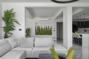 A modern living room with a sofa, a large potted plant, and a wall-mounted artwork. - 4 Bedroom Luxury Villa (Agios Nikolaos)
