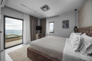 A modern bedroom with a large bed, a TV, a desk, and a view of the sea. - 4 Bedroom Luxury Villa (Agios Nikolaos)