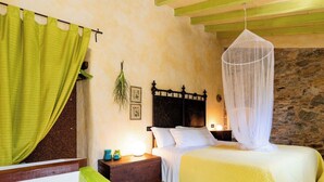 Ein Schlafzimmer mit einem Bett, einem Nachttisch, einer Lampe, einem grünen Vorhang und einer Steinwand.