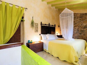 Ein Schlafzimmer mit einem Bett, einem Nachttisch, einer Lampe, einem grünen Vorhang und einer Steinwand.