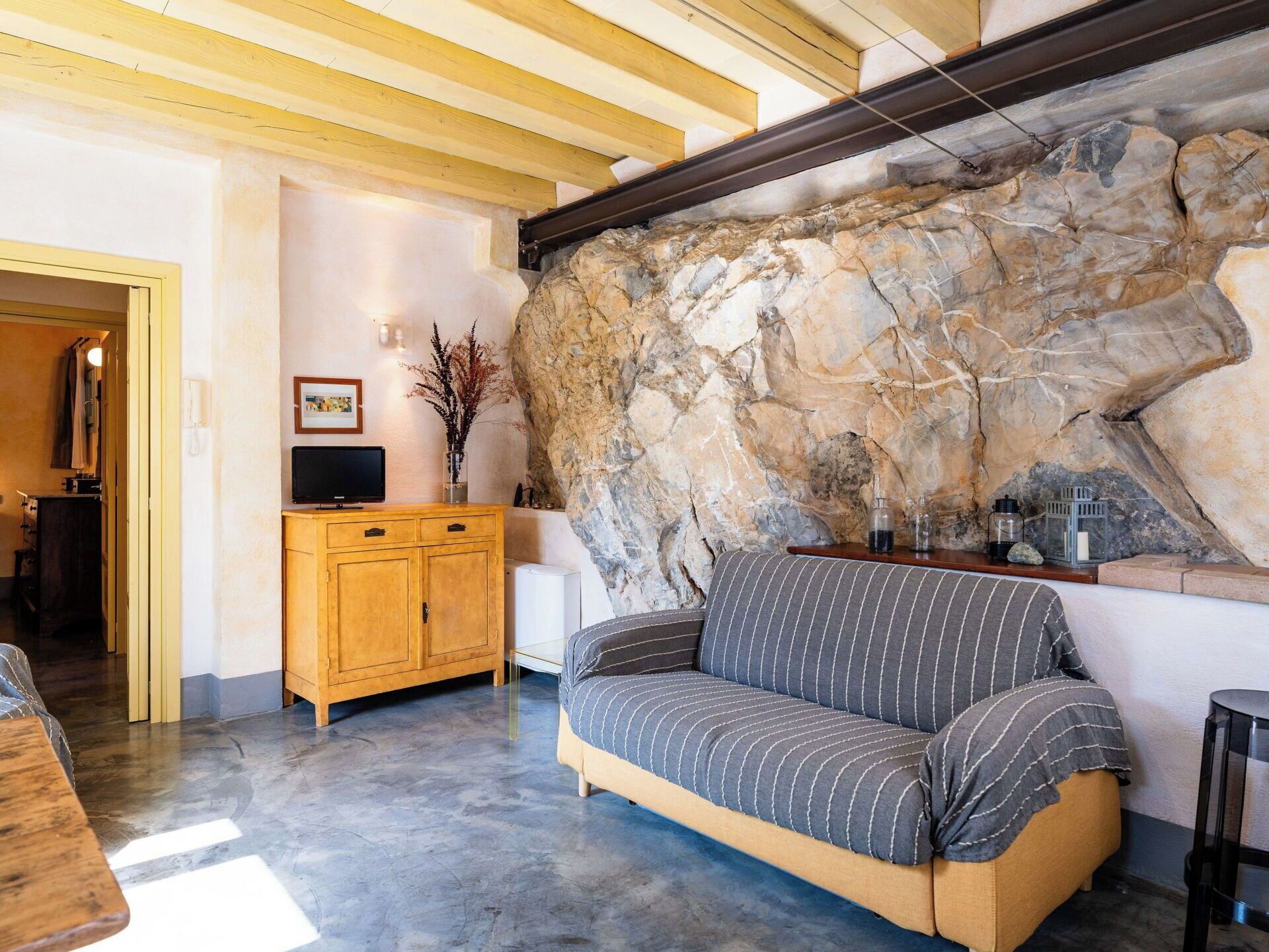 Una sala de estar con pared de piedra, un mueble de madera, un televisor y un sofá a rayas.