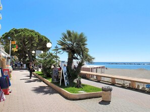Une promenade en bord de mer avec un sentier pavé, des palmiers et une plage en arrière-plan.