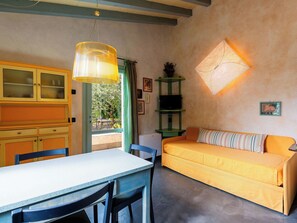 Ein Zimmer mit Esstisch, Stühlen, einer Couch, einer grünen Regaleinheit und einer Wandleuchte.