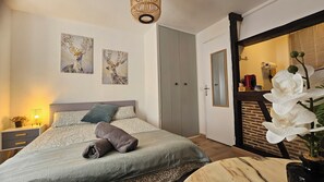 A bedroom with a bed, two wall-mounted paintings, a bedside lamp, a nightstand, a dresser, a door, and a potted orchid. - Quiet studio 2 pers hyper-centre - Cathedral (Orléans)