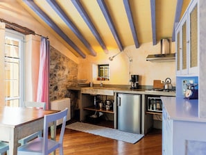 Eine kompakte Küche mit Steinwand, Holzbalken, Spüle, Kühlschrank und Herd.