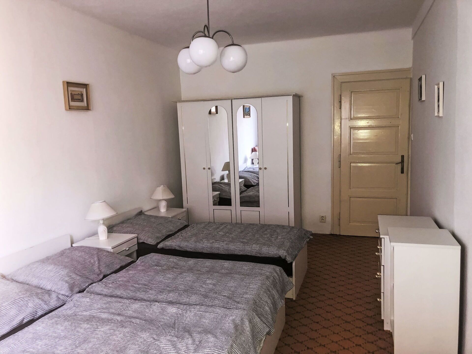 A bedroom with two beds, a wardrobe, a mirror, a door, and a lamp.