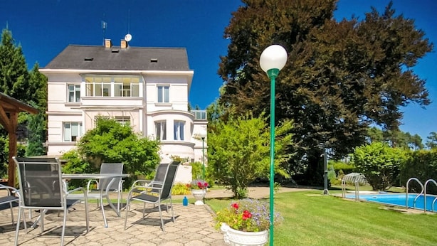 Ein Haus mit Terrasse, Sitzgelegenheiten im Freien, einem Swimmingpool und einem großen Baum.
