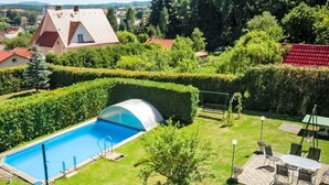 Ein Schwimmbad mit Glasüberdachung, umgeben von gepflegten Hecken und einer Terrasse mit Gartenmöbeln.