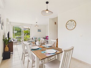 A dining area with a wooden table, white chairs, and a view through glass doors to an outdoor space. - Near sea – Charming house with garden – Sleeps 6 (Fréhel)