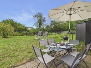 Ein Essbereich im Freien mit Tisch, Stühlen, einem großen Sonnenschirm und einem Grill.