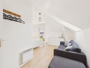 A modern bedroom with a loft-style ceiling, a bed, a gray sofa, and a white dresser. - Near sea – Charming house with garden – Sleeps 6 (Fréhel)