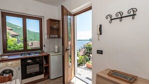 A kitchen with a stove, oven, and washing machine, a wooden cabinet, and a view of a lake through an open door. - Beautiful apartment for 2 guests with WIFI, TV and terrace (Mergozzo)