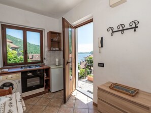 Una cucina con piano cottura, forno e lavatrice, un armadietto in legno e vista su un lago attraverso una porta aperta.