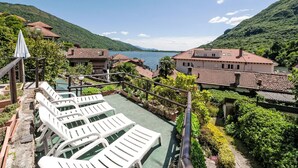 A terrace with white lounge chairs, a pool, and a view of a lake and mountains. - Beautiful apartment for 2 guests with WIFI, TV and terrace (Mergozzo)