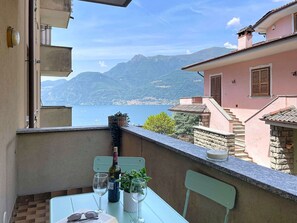 Ein Balkon mit Tisch, zwei Stühlen, einer Weinflasche, zwei Weingläsern, einem Buch und einem Blumentopf.